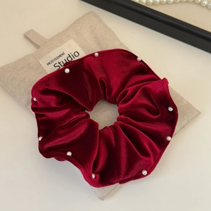 Detailed close-up of dark red velvet scrunchie with pearls next to a linen pouch