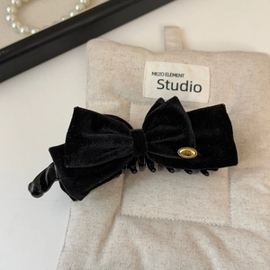 Detail of elegant black velvet bow banana clip with gold emblem on fabric background