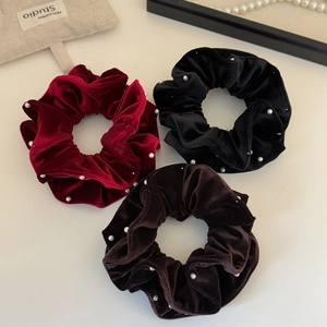 Close-up of three premium velvet scrunchies with white pearls in burgundy black and brown