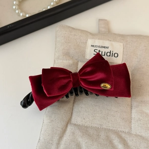Close-up of vintage red velvet bow hair clip with gold metal logo and black claw clip detail