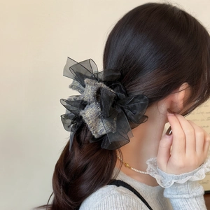 Close-up of black mesh scrunchie with tweed fabric accent worn on a low ponytail