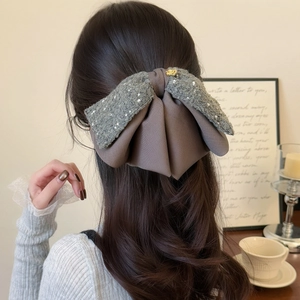 Elegant grey tweed and brown satin bow hair clip shown on a hairstyle in a cozy setting