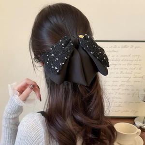 Elegant black tweed bow hair clip with gold metal accent shown on model's hair