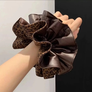 Fashionable leopard print and dark brown leather oversized scrunchie on a model's wrist