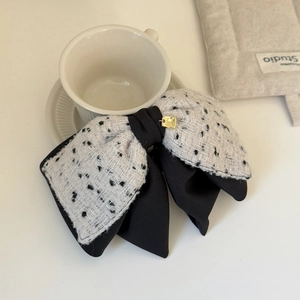 Close-up of a tweed bow hair clip featuring an engraved good luck gold square charm