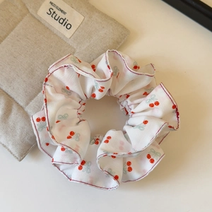 Detailed view of white chiffon scrunchie with sweet red cherry and blue bow patterns