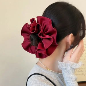 Deep red satin scrunchie with layered ruffles shown on a high bun hairstyle