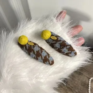 Detail of houndstooth knit hair clips with yellow pom poms and Love letter labels