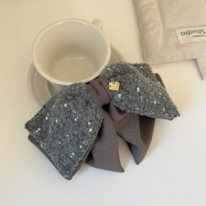 Detail of elegant knit bow hair clip featuring textured grey fabric and gold metal accent
