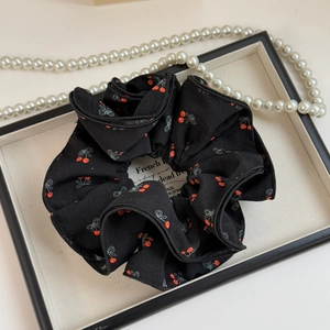 Gros plan du chouchou noir oversize à motifs cerises rouges sur tissu plissé doux