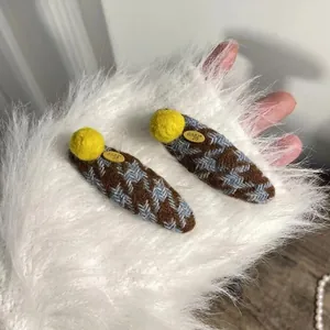 Knitted houndstooth hair clip with yellow plush ball and Love tag on fuzzy white background