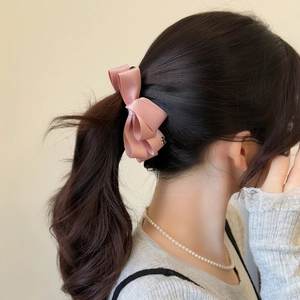 Detail showing pink satin layered bow hair clip worn on a high ponytail for women