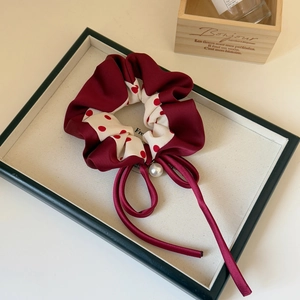 Close-up of wine red polka dot scrunchie with hanging pearl and long ribbon tails