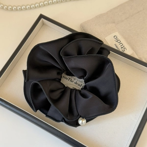 Detail of elegant black satin scrunchie with a refined pearl pendant on a display tray