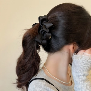 Detailed back view of an elegant black satin bow banana clip on long brown wavy hair
