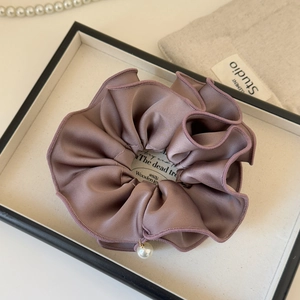 Detail of a brown satin scrunchie with silk luster, finished edges, and a pearl pendant