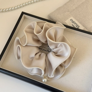 Close-up of beige satin scrunchie with delicate scalloped edges and a pearl pendant