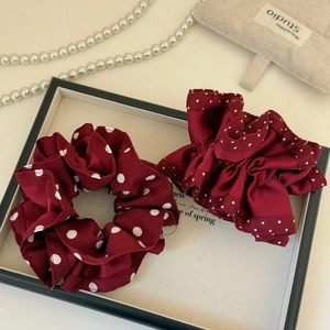 Detailed view of burgundy polka dot satin scrunchies on an elegant cream display tray