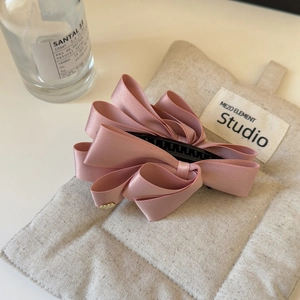Detailed view of pink satin layered bow hair clip on a soft textured fabric surface
