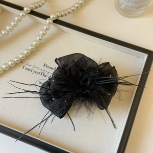 Macro shot of elegant black mesh hair clip with soft feathers and sparkling rhinestones