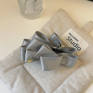 Detail of grey silk satin bow hair clip with a gold heart charm and layered fabric design
