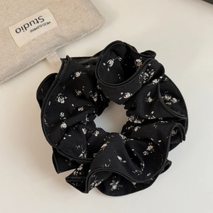 Detailed close-up of a black floral fabric scrunchie with soft ruffled chiffon texture