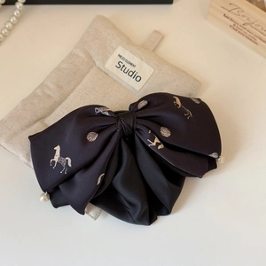 Detailed close-up of a black satin bow hair clip with horse print and pearl accents
