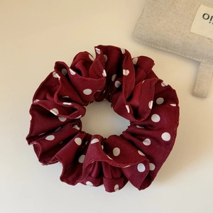 Detailed view of burgundy red satin hair scrunchie with white polka dots texture