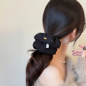 Detail of knitted black scrunchie on hair with Hand Made label and gold charm