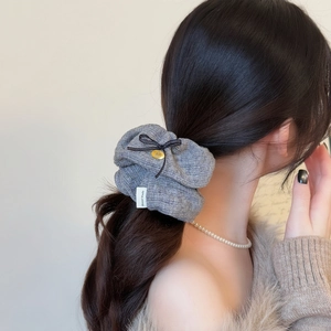 Grey knitted textured scrunchie with bow and gold charm accessory on ponytail