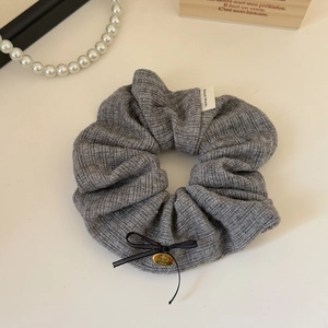 Detail of grey knitted scrunchie with a Hand Made label and golden cherry charm