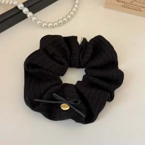 Detail of black knitted scrunchie with a gold cherry pendant and white handmade label