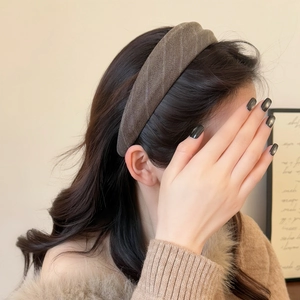 Détail d'un serre-tête en tissu rayé gris-brun porté par un mannequin sur fond beige