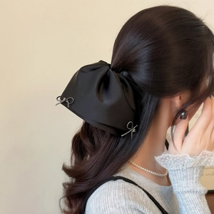 Detail view of a large black satin bow hair claw with elegant silver diamond butterfly accents