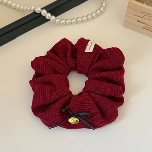 Close-up of knit fabric scrunchie with bow and gold cherry pendant on table