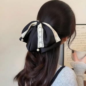 Elegant black satin bow hair claw with white lace trim and pearls worn by a model