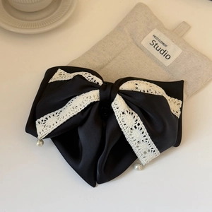 Detailed close-up of a black satin bow hair clip with white lace and pearl pendants