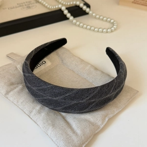 Gros plan d'un serre-tête en tissu gris foncé à rayures sur un sac en lin beige