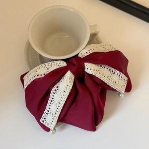 Detailed view of burgundy satin bow hair claw with white lace trim and pearl pendants