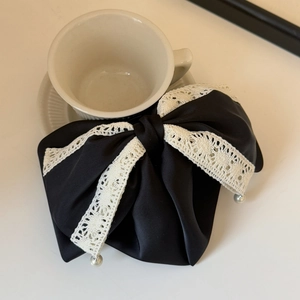 Close-up of black satin bow hair clip with beige lace trim and pearl accents on desk