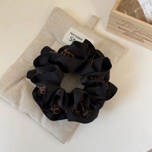 Détail du chouchou en soie noire et imprimé léopard avec volants sur lin beige