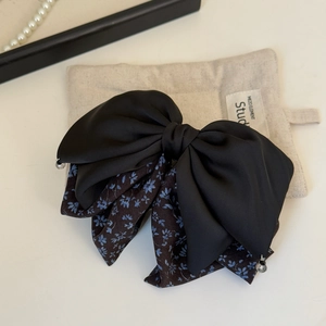 Detail of floral and black satin bow hair clip with crystal beads on a soft linen pouch