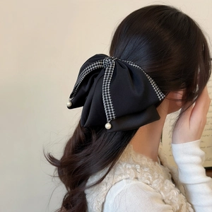 Detail of large black fabric bow hair claw with houndstooth trim and pearl accents
