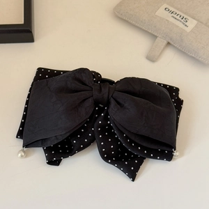 Detail of a double-layered black polka dot bow hair clip with elegant pearl accents
