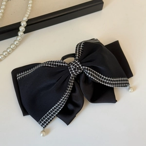 Detail of elegant black satin bow hair claw with houndstooth trim and pearl charms