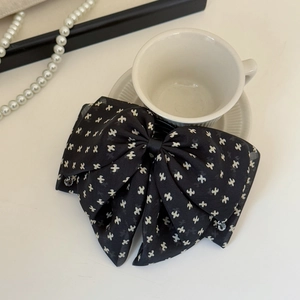Elegant black bow hair clip with white pattern shown with pearls and coffee cup