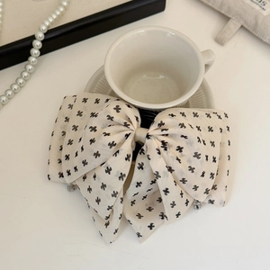 Detail of oversized cream bow hair claw with black cross pattern and metal spring clip