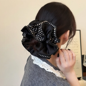 Detail of black satin scrunchie with checkerboard trim worn on a low bun hairstyle