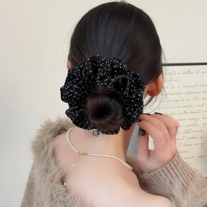 Détail d'un chouchou floral avec pendentif doré sur une coiffure élégante en queue de cheval