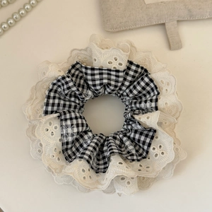 Detailed close-up of lace-trimmed black and white plaid scrunchie on a white surface